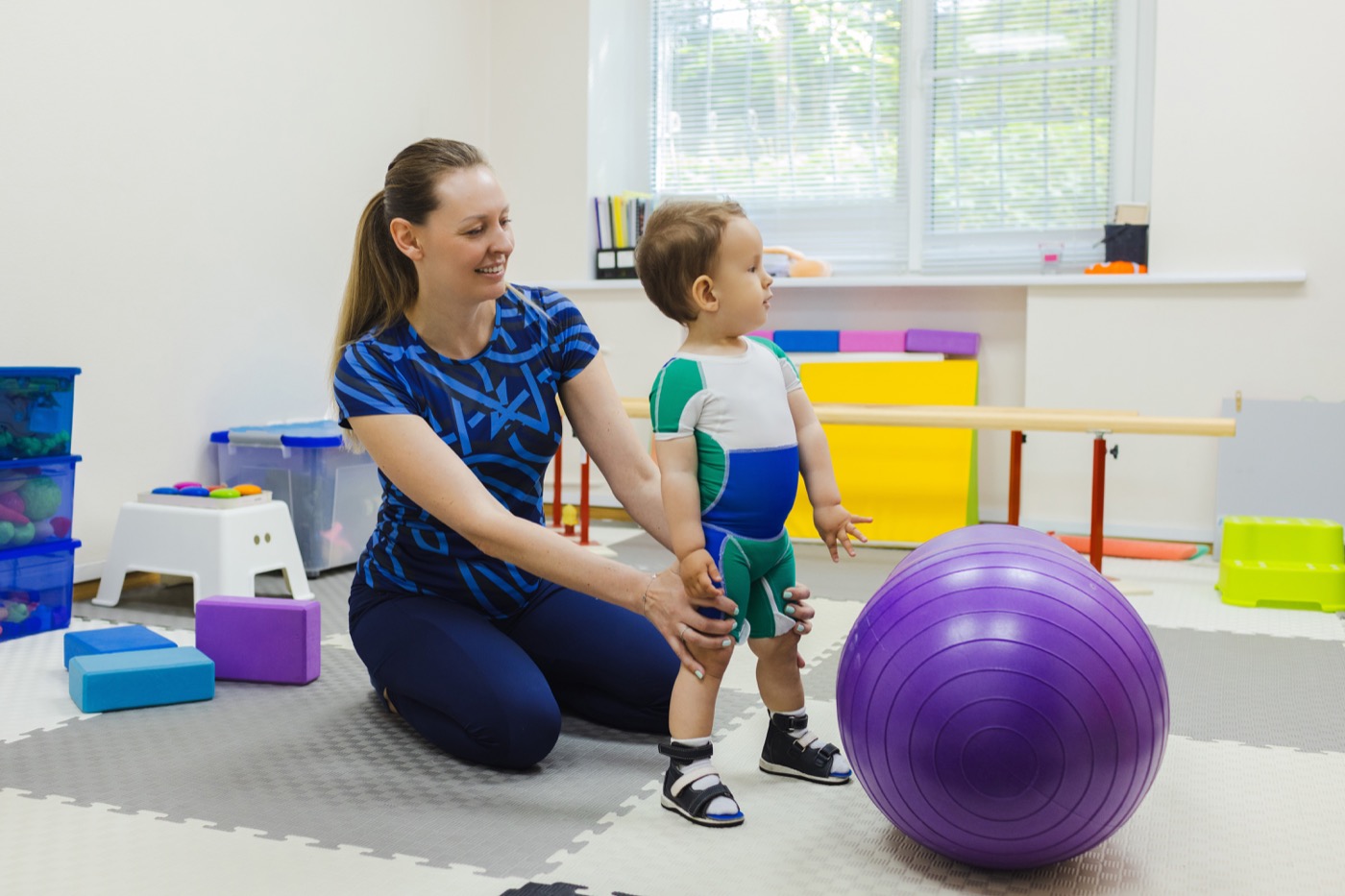 Pediatric physical therapist working with a toddler and exercise ball during a session